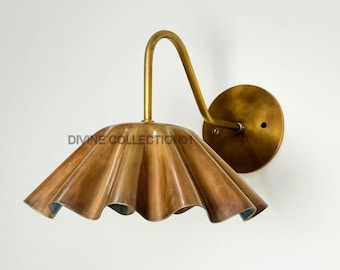 May include: A brass wall sconce with a ruffled, petal-shaped shade. The fixture has a curved arm and a circular backplate. The text "DIVINE COLLECTION01" is printed on the shade.