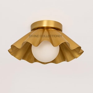 May include: A gold-coloured ceiling light fitting with a ruffled shade and a spherical white light. The fitting has the text "DIVINE COLLECTION01" on the shade.