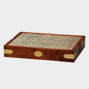 May include: A rectangular wooden tray with a dark brown finish. The tray features a gold-colored, patterned surface and decorative gold-colored metal accents on the corners and sides. An oval gold-colored emblem is centered on the front.