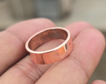 May include: A copper-colored ring with a flat band. The ring is held in a hand, showcasing its simple, yet elegant design. The ring's color is a warm, reddish-brown hue, suggesting a vintage or handcrafted aesthetic. This ring is a piece of jewelry.