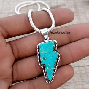 May include: A silver necklace featuring a turquoise lightning bolt pendant. The pendant has a textured, bright blue-green stone set in a silver frame with a twisted rope design. The chain is a silver snake chain.
