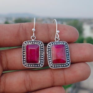 Puede incluir: Un par de pendientes de plata con piedras preciosas rectangulares de color rojo intenso. Las piedras están engastadas en un marco de plata con un borde de cuentas. Cierre de gancho sencillo.