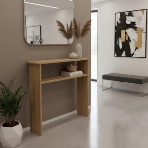 Puede incluir: Una consola de roble claro con un estante inferior, coronada por un espejo y un jarrón decorativo. La habitación presenta una estética moderna con una paleta de colores neutros y una planta en maceta geométrica.