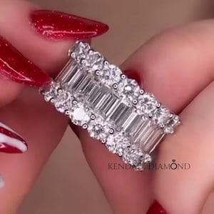 May include: A silver ring with multiple rows of clear, sparkling gemstones. The ring features a combination of baguette and round-cut stones, creating a dazzling display. The text "Kendall Diamond" is visible on the ring.