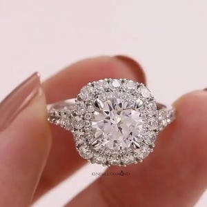 May include: A silver-toned ring featuring a large round-cut centre stone surrounded by a double halo of smaller round-cut stones. The band is split and encrusted with additional small stones. The text KENDALL DIAMOND is printed below the ring.