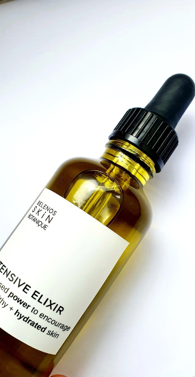 May include: A clear glass bottle of skincare product with a black dropper. The bottle contains a golden-colored liquid. The label reads "BELENOS SKIN BOTANIQUE" and "INTENSIVE ELIXIR". The product is designed to encourage healthy and hydrated skin.