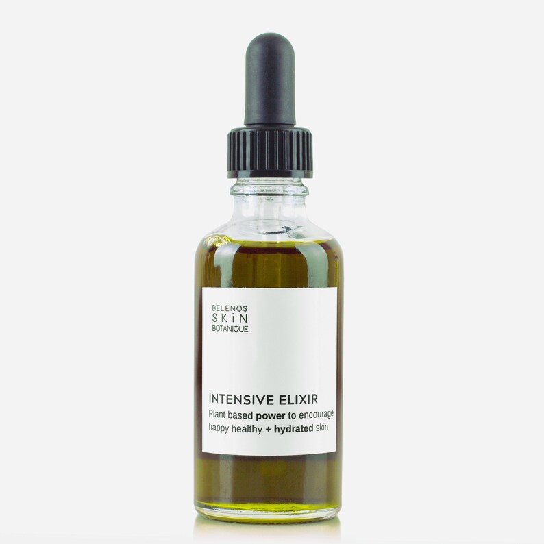 May include: A clear glass bottle of Intensive Elixir skincare product. The bottle has a black dropper and a white label with the brand name and product information. The liquid inside is a golden-green color.