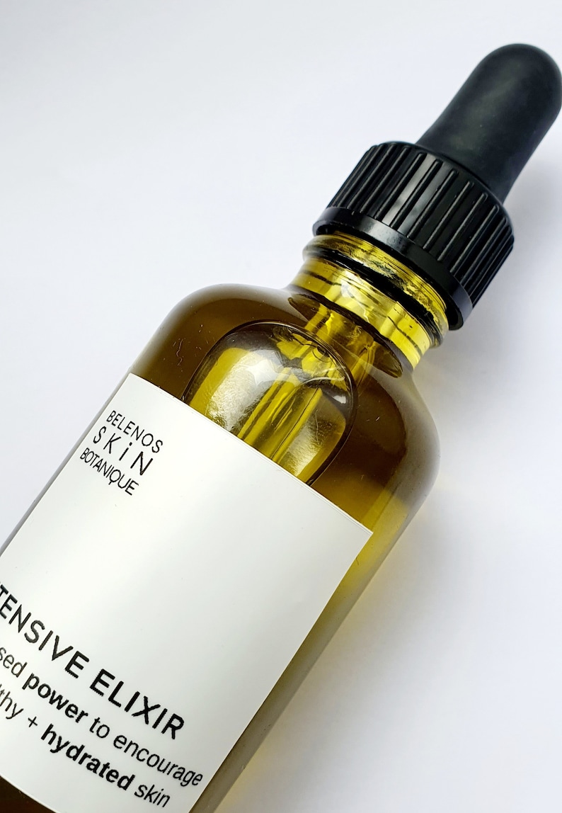 May include: A close-up of a skincare product bottle. The bottle is olive-green glass with a black dropper and cap. A white label displays the brand name and product description. The bottle is filled with a golden liquid.