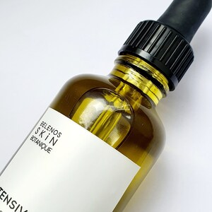 May include: A clear glass bottle of skincare product with a black dropper. The bottle has a white label with the text "BELENOS SKIN BOTANIQUE" and "INTENSIVE ELIXIR". The product is a yellow liquid.