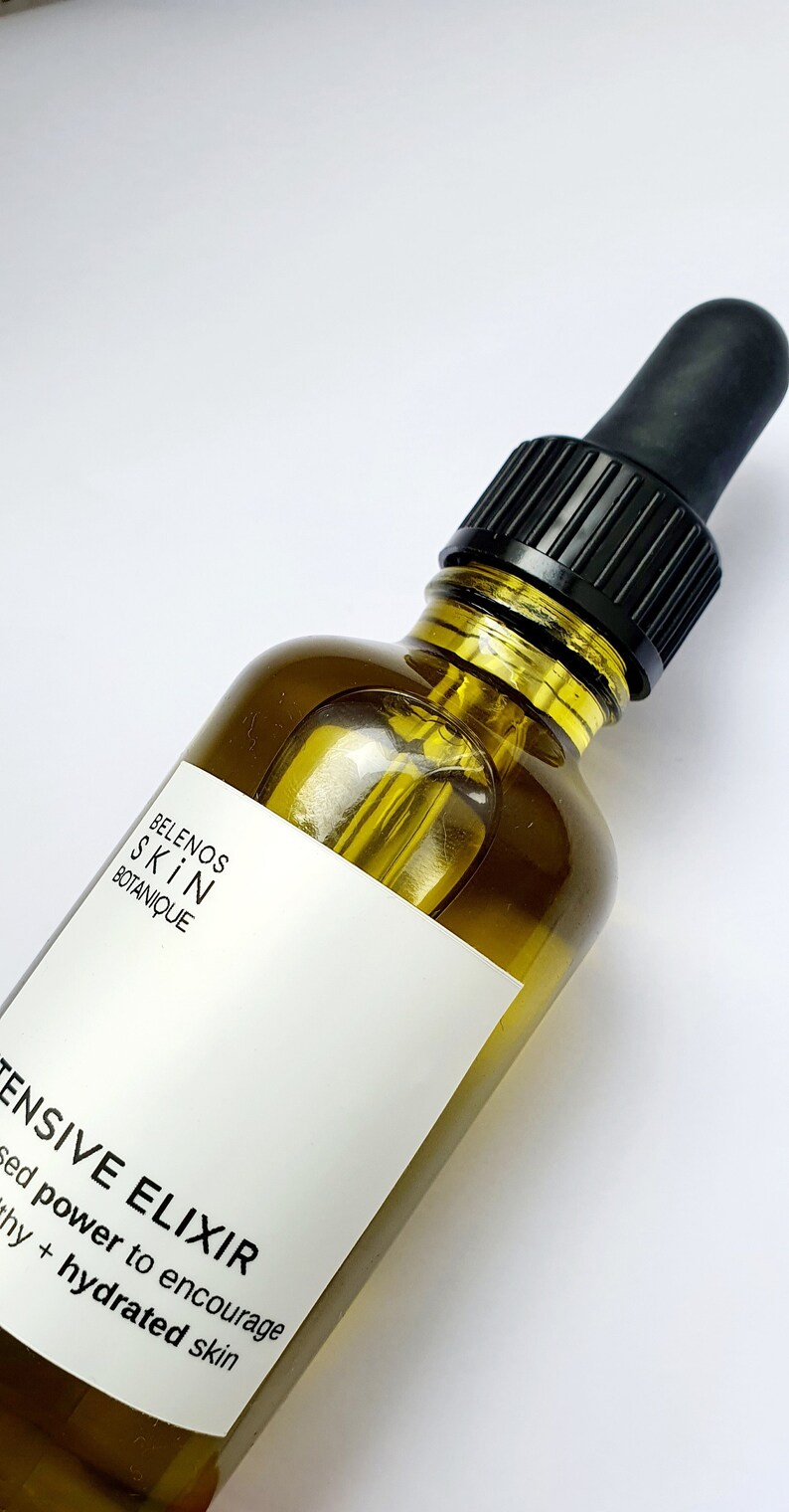 May include: A clear glass bottle of skincare product with a black dropper. The bottle has a white label with the text "BELENOS SKIN BOTANIQUE" and "INTENSIVE ELIXIR". The product is a yellow liquid.