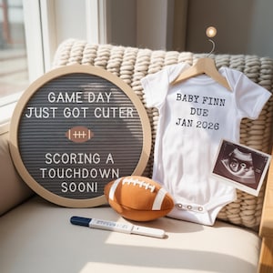 Puede incluir: Anuncio de embarazo con un body blanco con la frase "BABY FINN DUE JAN 2026", una pizarra de fieltro con "GAME DAY JUST GOT CUTER SCORING A TOUCHDOWN SOON!", un balón de fútbol americano de peluche y una ecografía.