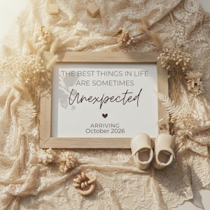 May include: A framed print with the text "THE BEST THINGS IN LIFE ARE SOMETIMES Unexpected" and "ARRIVING October 2026". The image includes baby shoes, a wooden toy, and decorative flowers on a lace background.