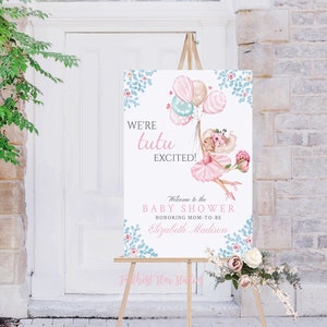 May include: A pink and blue baby shower welcome sign with a cartoon ballerina holding balloons. The sign reads "We're tutu excited!" and "Welcome to the Baby Shower Honoring Mom-to-be Elizabeth Madison".
