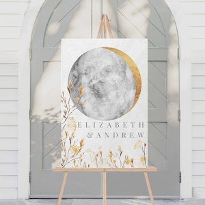 Pode incluir: Um sinal de boas-vindas de casamento com uma lua em aquarela e detalhes dourados. O sinal diz "Elizabeth & Andrew" e é exibido em um cavalete de madeira.