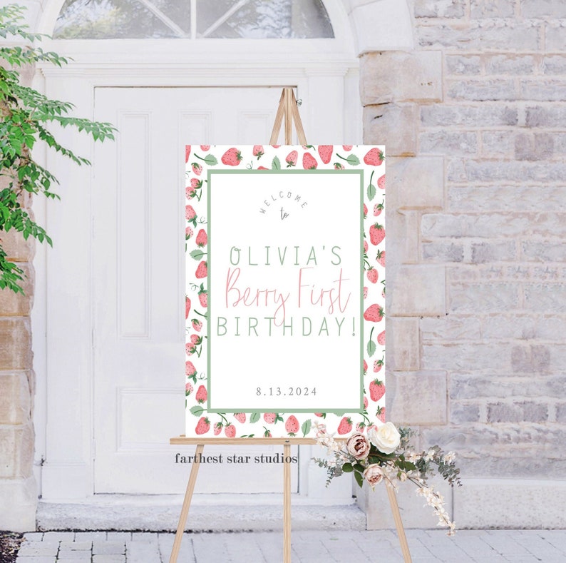 May include: Welcome to Olivia's Berry First Birthday! A white sign with a green border and a strawberry pattern. The text is in pink and green. The date 8.13.2024 is printed below the text. The sign is on an easel.