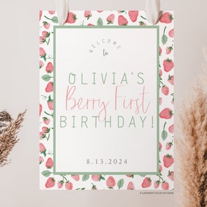 May include: A white welcome sign with a green border and a strawberry pattern. The sign says "Welcome to Olivia's Berry First Birthday! 8.13.2024"