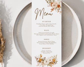 Op de afbeelding: Een herfstmenu met een bloemmotief met pompoenen, bladeren en bessen. Het menu bevat voorgerechten, hoofdgerechten, bijgerechten en desserts. De tekst luidt: "Menu, Voorgerecht, Pompoensoep met crème fraîche, Prosciutto-gewikkelde vijgen, Assortiment brood en kaas, Hoofdgerecht, Kruiden-gekorst lamsrack, Gebakken zalm met citroensaus, Filet mignon met hollandaisesaus, Bijgerechten, Gebakken aardappelen met tijm, Zoete aardappelen met marshmallows, Groene bonen met sjalotten, Dessert, Klassieke tiramisu, Pompoen cheesecake, Diverse taarten, FARTHEST STAR STUDIOS."