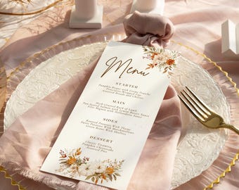 Op de afbeelding: Een menukaart met bloemaccenten en het woord "Menu" in een elegant lettertype. De kaart ligt op een decoratieve bord met een gouden rand, een roze servet en een gouden vork. Het menu bevat voorgerechten, hoofdgerechten, bijgerechten en desserts.