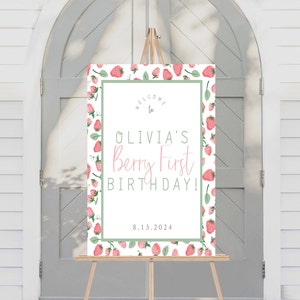 May include: Welcome to Olivia's Berry First Birthday! A white welcome sign with a green border and a strawberry pattern. The text is in black and pink. The date 8.13.2024 is printed at the bottom.