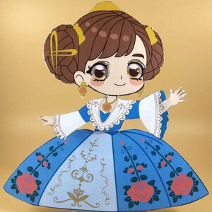 May include: A paper doll in a blue dress with a floral design and a white bodice. The doll has brown hair styled in a bun, gold earrings, and a gold necklace. The doll is in a welcoming pose.