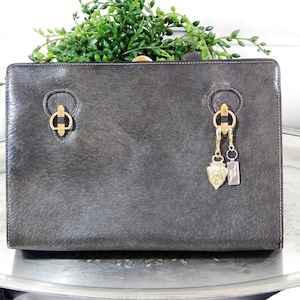 May include: A dark gray leather handbag with gold hardware and a gold charm attached to the handle.