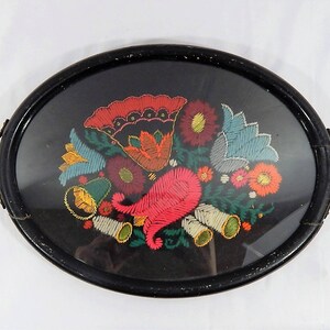 May include: An oval wooden tray with a black painted finish and brass handles. The tray features a colorful embroidered floral design with red, pink, yellow, blue, and green flowers.