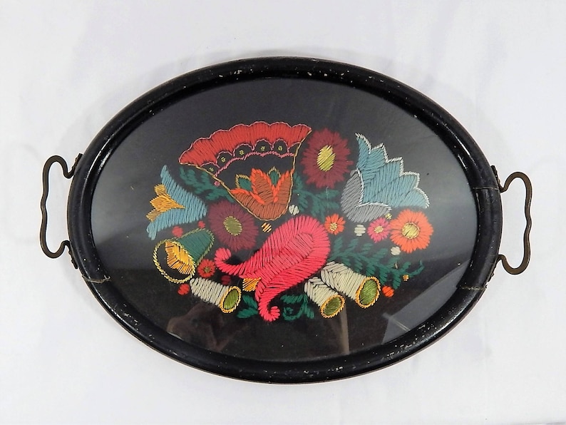 May include: An oval wooden tray with a black painted finish and brass handles. The tray features a colorful embroidered floral design with red, pink, yellow, blue, and green flowers.