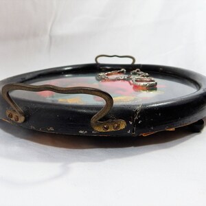 May include: A black wooden tray with a gold handle and a floral design. The tray has a glass insert with silver rings.