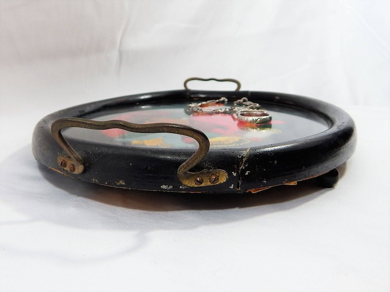 May include: A black wooden tray with a gold handle and a floral design. The tray has a glass insert with silver rings.