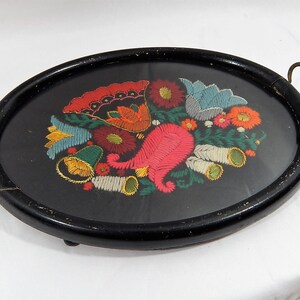 May include: A black oval tray with a gold handle. The tray is decorated with a colorful embroidered floral design.