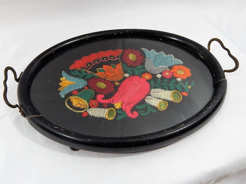May include: A black oval tray with a gold handle. The tray is decorated with a colorful embroidered floral design.