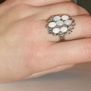 Könnte beinhalten: Ein silberner Ring mit einem Cluster aus weißen Opal-Steinen, die in einem floralen Design gefasst sind.