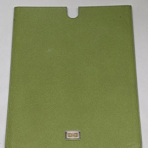 Może przedstawiać: Prostokątne, oliwkowozielone etui na tablet z zaokrągloną górą i małym prostokątnym emblematem na dole. Etui ma teksturowaną powierzchnię i wycięcie u góry.