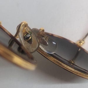 May include: Close-up of sunglasses with a gold frame and dark lenses. The nose pads are clear and the frame has a tortoiseshell pattern. The sunglasses are angled, showing the details of the frame and lenses.