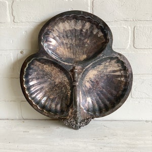 May include: A silver serving tray with three sections shaped like seashells. The tray has a decorative handle with a floral design.