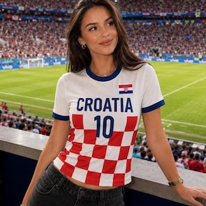 May include: A white and blue Croatia soccer jersey with the word "CROATIA" and the number "10" printed on it. The jersey has a red and white checkered pattern on the lower half and is worn at a soccer stadium.