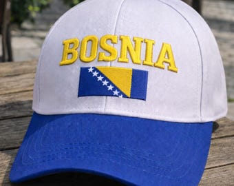 Puede incluir: Gorra de béisbol blanca y azul con la palabra "BOSNIA" bordada en amarillo. La gorra presenta la bandera de Bosnia y Herzegovina. La visera es azul y el botón superior es azul.