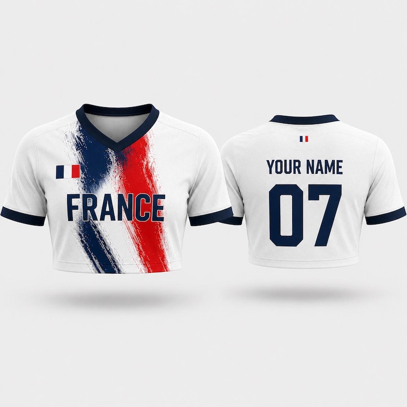 Puede incluir: Una camiseta corta blanca con cuello en V y ribetes azul oscuro. El frente presenta un dise&ntilde;o de pinceladas azules y rojas, la palabra FRANCE y una bandera francesa. La parte posterior muestra el texto YOUR NAME sobre el n&uacute;mero 07 y una bandera.