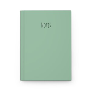 May include: A mint green notebook with the word "NOTES" in black script. The notebook has a clean, minimalist design, with a solid color cover and a simple, elegant font.