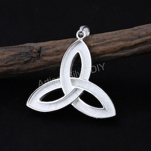 May include: A silver Celtic knot pendant, or triquetra, with a loop for a chain. The pendant is set against a dark background with a piece of wood. The text "Artistic DIY" is visible.