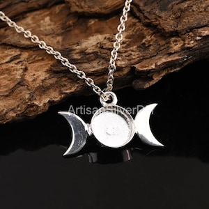 May include: A silver-toned necklace featuring a triple moon pendant. The pendant has a central circular setting flanked by two crescent moons. The chain is delicate, and the necklace is set against a dark, textured background.