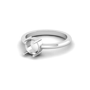 May include: A polished silver-toned ring featuring a circular setting with four prongs designed to hold a gemstone. The band is smooth and rounded, showcasing a clean, metallic finish that reflects light across its entire surface structure.