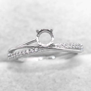 Puede incluir: Un anillo plateado con un engaste redondo y una banda dividida. Un lado de la banda está adornado con pequeñas piedras transparentes. El diseño del anillo presenta un estilo moderno y elegante, adecuado para diversas ocasiones.