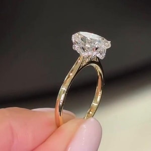 Könnte beinhalten: Ein goldener Ring mit einem großen, birnenförmigen Diamanten. Der Diamant ist klar und funkelnd, gefasst auf einem Band mit filigranem Design. Der Ring wird vor einem dunklen Hintergrund präsentiert.