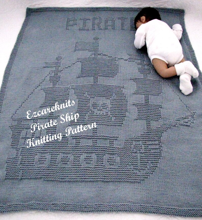 K&ouml;nnte beinhalten: Eine graue gestrickte Babydecke mit einem gestrickten Piratenschiff-Design. Die Decke hat das Wort "Pirate" in die Oberseite der Decke gestrickt. Die Decke liegt auf einer wei&szlig;en Oberfl&auml;che.