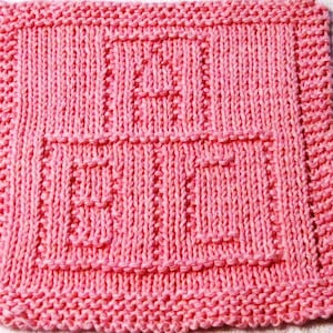 May include: A pink knitted dishcloth with the words "Make It" in a simple, blocky font.