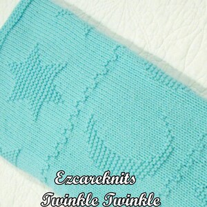 May include: A light blue knitted blanket with a star pattern. The blanket has the text "Ezcareknits Twinkle Twinkle" in a decorative font. The blanket is made of a soft, textured material.