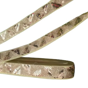 Può includere: Un rotolo di nastro decorativo con un design di paillettes. Il nastro è di colore oro chiaro con un motivo ripetuto di piccole paillettes. Il nastro è arrotolato nella parte inferiore dell'immagine.