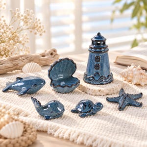 May include: A set of six blue ceramic nautical figurines including a lighthouse, an open seashell, a whale, a dolphin, a sea turtle, and a starfish. Each piece features a glossy, mottled blue glaze with dark blue detailing on the edges and features.