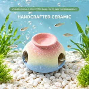 May include: A handcrafted ceramic fish hideout featuring a gradient colour scheme transitioning from pink at the top to yellow in the middle and blue at the bottom, with three circular openings and a speckled texture throughout the surface.